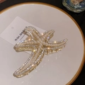 Elegant gold starfish hair claw clip with inlaid pearls and rhinestones on a white plate - Gold