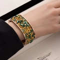 Detailed view of a wide gold cuff bracelet featuring vibrant green and amber crushed stones - Green