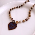 Détail macro du collier rétro avec perles et pendentif cœur en cuir sur assiette blanche - Coeur Café