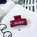 Close-up of a glossy red rectangular hair claw clip resting on a white decorative book - Rose Pink