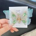 Mint green butterfly hair clip with shimmering rhinestones and tassels in a hand-held view - Green Wing Hair Clip (F0004) / Green
