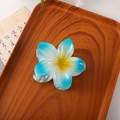 Blue gradient frangipani hair claw clip with yellow center on a wooden tray - Gradient Blue