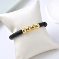 Close-up of black disc beads and gold spherical beads bracelet on white display pillow - Black & Gold Fashion / Black Disc / Gold Beads