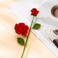 Detailansicht einer handgefertigten Häkelrose in Rot mit grünen Blättern und Textur - Rot