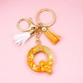 Detail of resin letter Q keychain with orange flakes and gold glitter on pink background - Letter Q