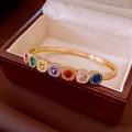 Macro view of a gold-plated bangle with seven colorful gemstones on a beige jewelry box - Gold Colored Gemstone Rainbow Bangle (7#)
