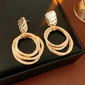 Detalle de pendientes de aro geométricos dorados con textura martillada en cuero negro - Dorado
