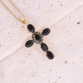 Dettaglio di un ciondolo a croce in oro con pietre di zircone nere su sfondo di pietra beige - Nero