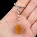 Llavero con colgante rectangular de piedra amarilla y cadena de plata en la mano - Topacio