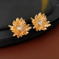 Macro shot of golden flower earrings with layered petals and a central zircon stone - Gold