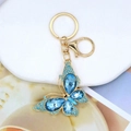 Detail of a gold butterfly keychain featuring blue rhinestones and crystals on a white stone - Butterfly 16