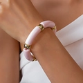 Nahaufnahme des Armbands mit hellrosa Acrylröhren und polierten Goldperlen am Handgelenk - Rosa