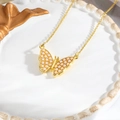 Detalle macro de un collar de mariposa bañado en oro con perlas sobre un plato cerámico - Mariposa Dorada Perla