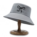 Gray bucket hat with black bow embroidery displayed on a wooden stand - Light Gray