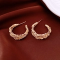 Détail de boucles d'oreilles créoles dorées avec texture tressée sur soie rouge - Or