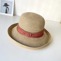 Close-up of a wide-brim straw sun hat with reddish-brown fabric ribbon on a white surface - Orange