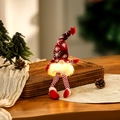 Close-up of a lit Christmas gnome with glowing beard and red snowflake hat on a table - Red Long Leg Style