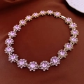 Primer plano detallado del collar floral dorado con piedras púrpuras sobre fondo de tela café - Collar Morado