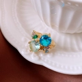 Dettaglio di anello geometrico con cristalli blu e verdi su base di porcellana bianca fine - Oro-Blu-Viola