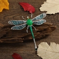 Spilla a libellula con ali in smalto verde e occhi con gemme rosse su fondo legno - Libellula in Giada Artificiale Ali Blu / Blu