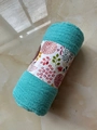 Teal voile scarf rolled with floral paper band on marble floor for a stylish presentation - Aqua Blue