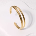 Bracciale rigido aperto a doppia linea in oro e acciaio inossidabile su base bianca moderna - Oro