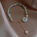 Detail of light green jade beads and white pearls bracelet on a champagne silk fabric - Green