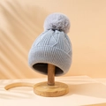 Light grey knitted beanie with fluffy pom pom on wooden stand under soft tree shadows - M(56-58cm) / Gray