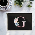 Black canvas cosmetic bag with floral letter G design on white marble surface - Letter G