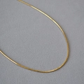 Collana choker minimalista in ottone dorato a molla su uno sfondo grigio materico - Oro