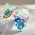 Detail of transparent bear keychain featuring blue liquid, glitter, and colorful beads - Gradient Strap + Bear / Blue
