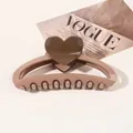 Detailed view of a coffee brown heart claw clip made of resin on a fashion magazine - Heart Hollow Semicircle / Coffee