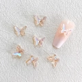 Macro shot of 3D iridescent resin butterfly charms on a pink manicured fingernail - Aurora Champagne