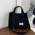 Bolso negro de pana con asas dobles y correa de hombro ajustable sobre mesa de madera - Negro