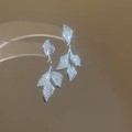 Détail de boucles d'oreilles feuilles en argent avec zircons étincelants sur support chaud - Argenté