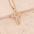 Dettaglio ravvicinato di una collana croce dorata con zirconi champagne su pietra beige - Champagne