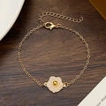 Elegant gold chain bracelet featuring a white shell flower pendant on a dark wood background - Gold White Resin Flower