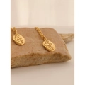 Detailed close-up of rose embossed golden oval pendant on a natural stone surface - Gold