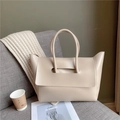 Minimalist beige leather tote bag with unique cutouts on a cozy sofa setting - Khaki