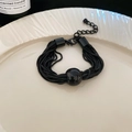 Detailansicht eines mehrlagigen schwarzen Kettenarmbands mit Metallperlen auf dem Teller - Armband - Schwarz