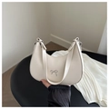 Detail of beige leather crescent bag with a decorative metal bow and slim shoulder strap - White