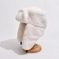 Winter-Plüschmütze mit Ohrenklappen in Cremeweiß aus Kunstfell auf einem Holzständer - Einheitsgröße / Gebrochenes Weiß