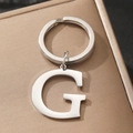 Silver metal alphabet G keychain with round ring on a textured golden surface - Letter G
