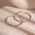 Detail of silver hoop earrings featuring a diamond-cut textured surface on a stone background - Silver Color Twisted Hoop (Silver Needle)