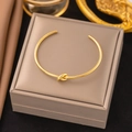 Minimalist golden stainless steel open knot bangle presented on a luxury jewelry box - Gold Knot Open Bangle (SLE105)