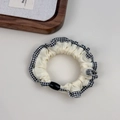 Detail of a beige fabric scrunchie featuring black plaid lace trim and a black bead accent - Off-white with Black & White Plaid