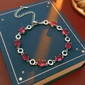 Detail eines Armbands mit roten ovalen Zirkonsteinen und silbernen Gliedern auf Buch - Silber - Rosarot