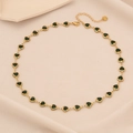 Elegant gold necklace featuring green heart-shaped gemstones on beige fabric background - Green