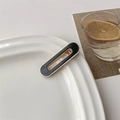 Close-up of a black resin hair clip with gold metal trim on a white ceramic plate - 7# Black Oval Hollow Out
