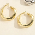 Detailed view of twisted gold hoop earrings with metallic luster on a beige textured surface - Smooth U-Shape / Gold